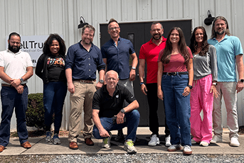 Ten diverse staff members of Well Trust Medical Group pose together outside their office building.